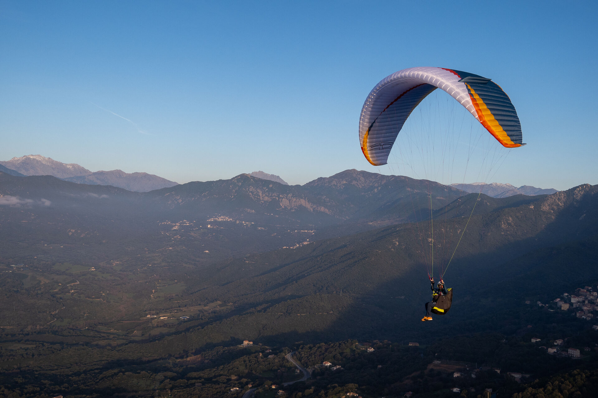 Paraglider soaring above golden mountain valleys at dusk